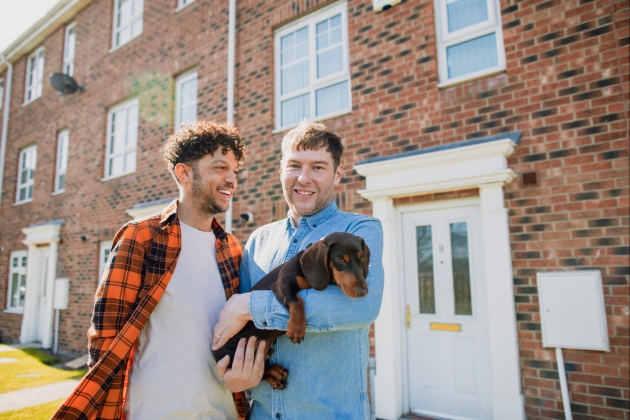 Man holds small dog with partner in front of house