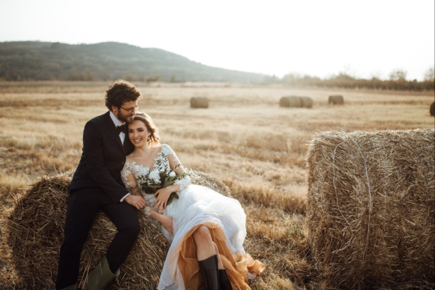 Newly married couple in their wedding outfits sitting on a haybale in a field