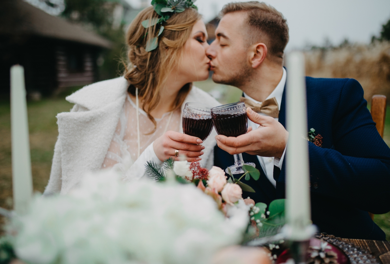 wedding couple outdoors seated kissing clinking glasses of red wine 