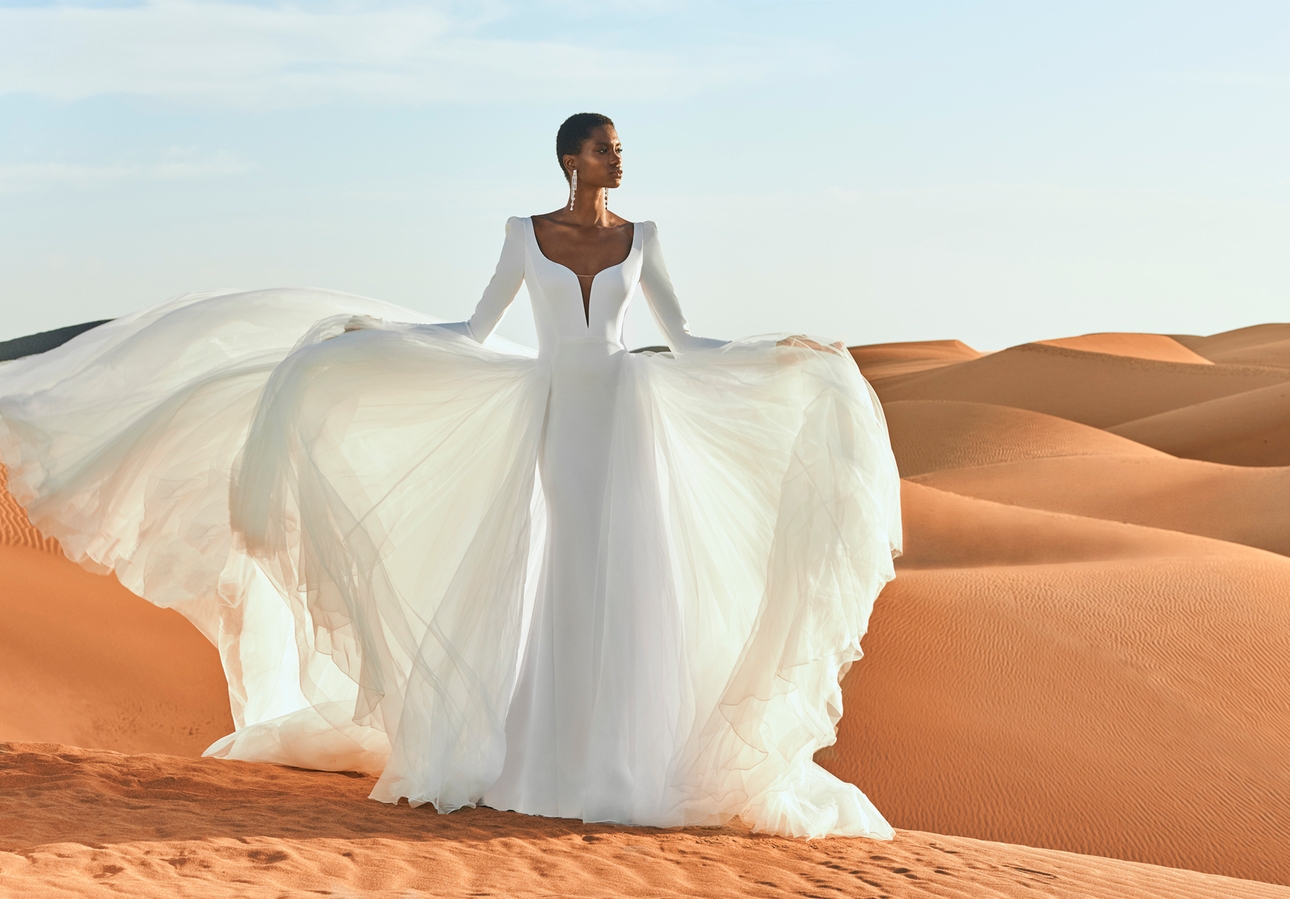Model wears dress from Pronovias Eden collection standing on the top of a sand dune