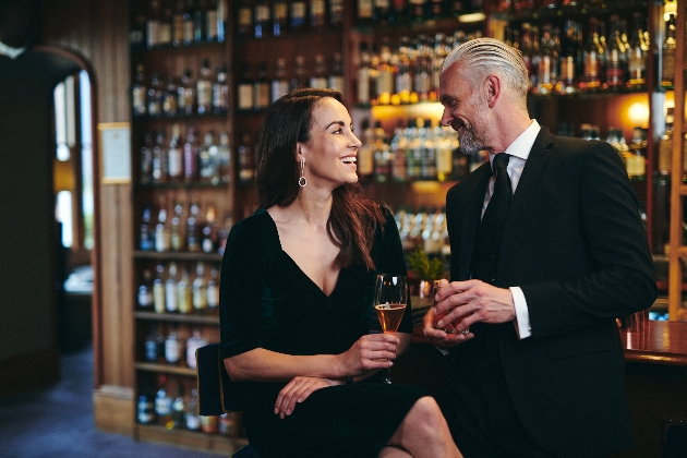 man and woman in black tie outfits sitting at a bar 