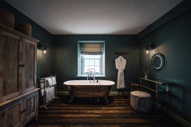 dark green bathroom with roll top freestanding gold bath in centre