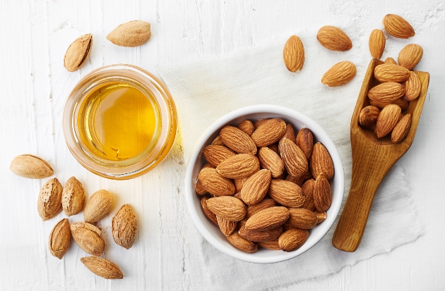 almonds in a pot with a jar of almond oil and a wooden scoop