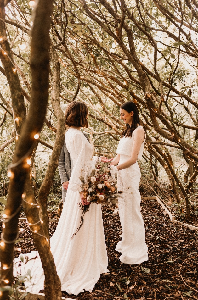 couple in wedding dresses standing in the woods getting married