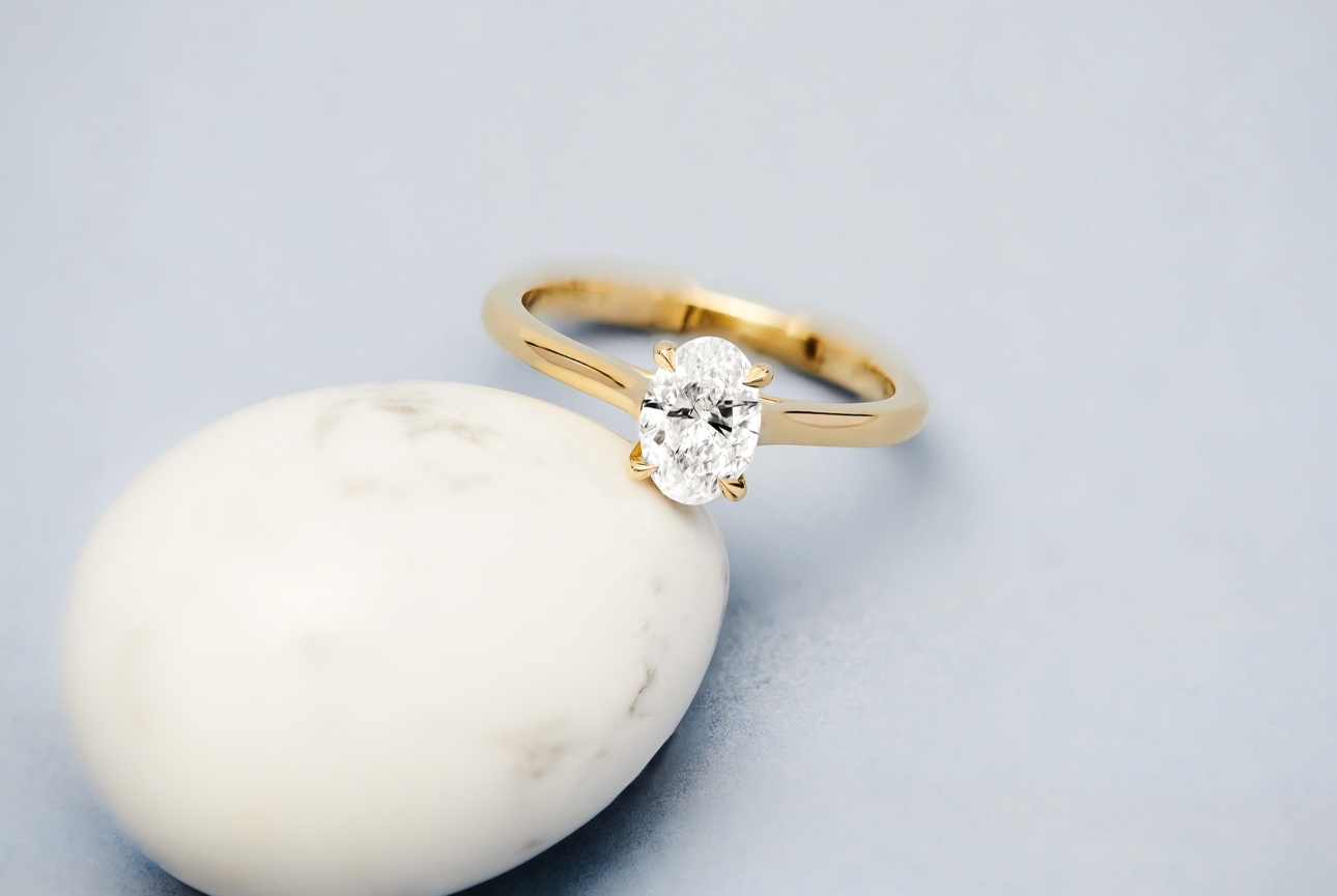 gold and diamond oval engagement ring lying on a rock