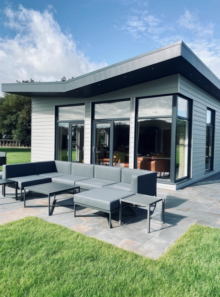 grey wooden modern bungalow with panoramic windows and a patio with table and chairs