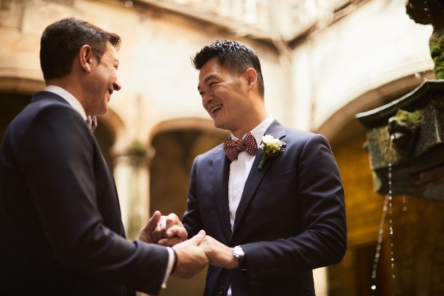 groom and groom holding hands by a water fountain