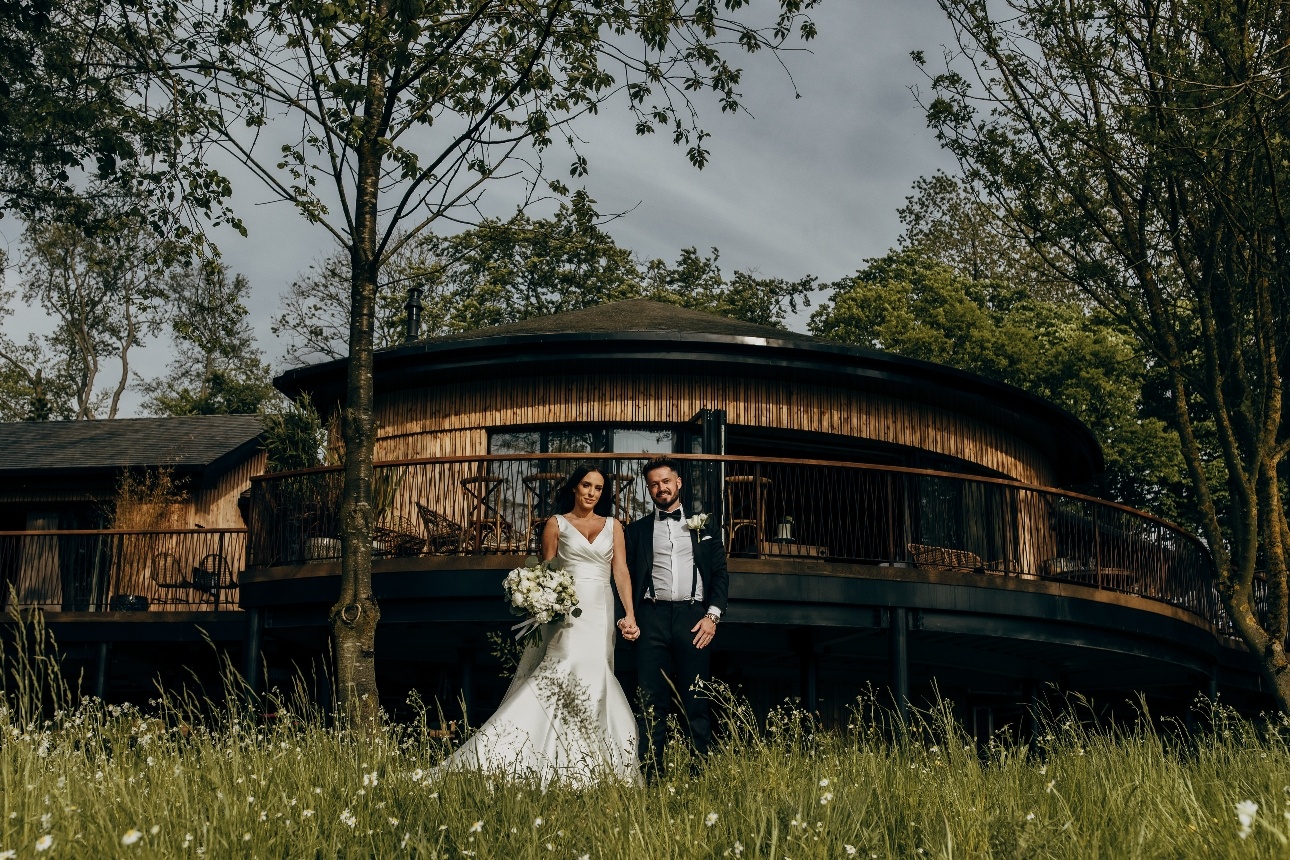 bride and groom standing on the grass in front of low rising tree house 