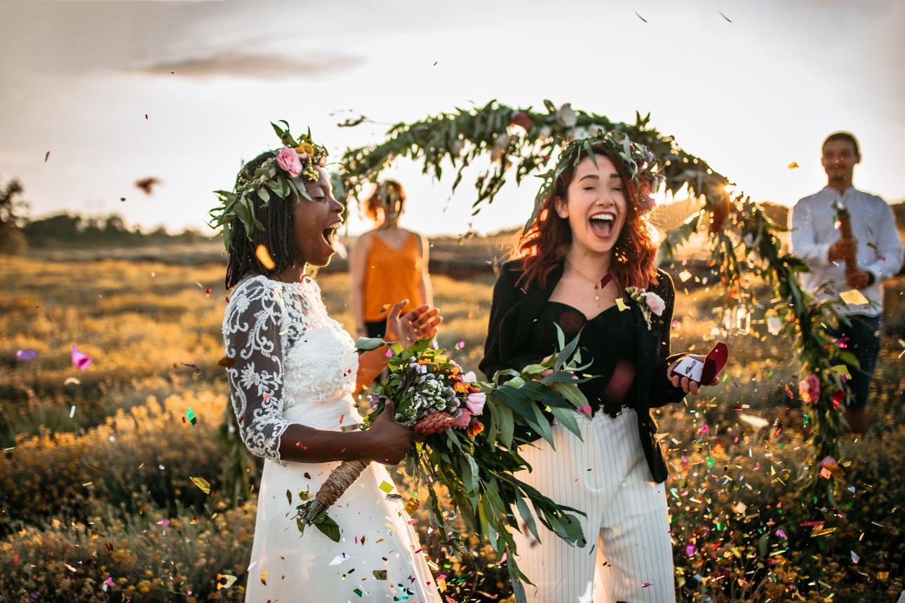 two women tying the knot out side under a flower arch