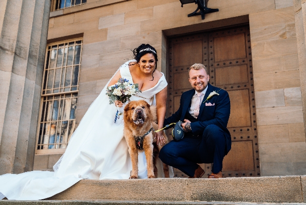 bride and groom on steps outside their wedding venue with their dog