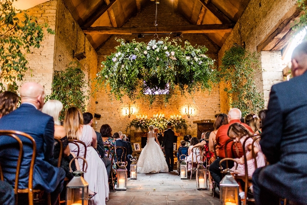 brick barn interior with floral hanging, guests lined up in aisles