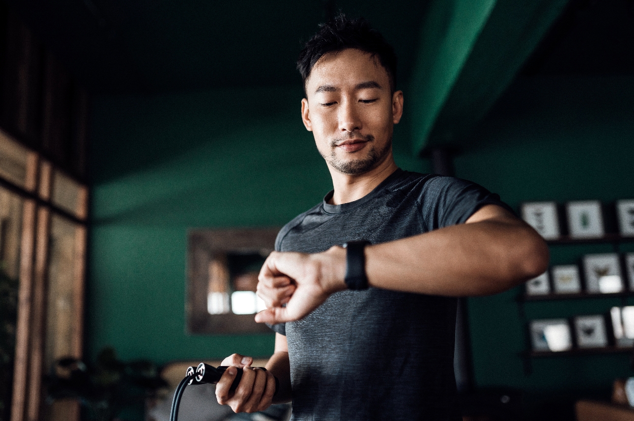 man at home exercising with skipping rope and looking at his watch