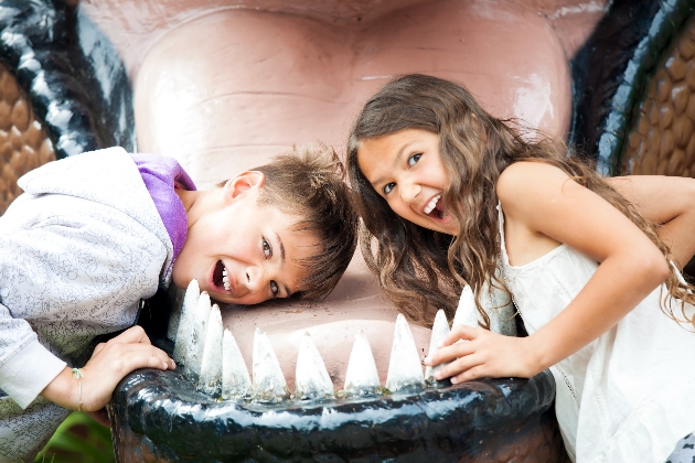 A boy and girl laughing with their head inside a toy dinosaur