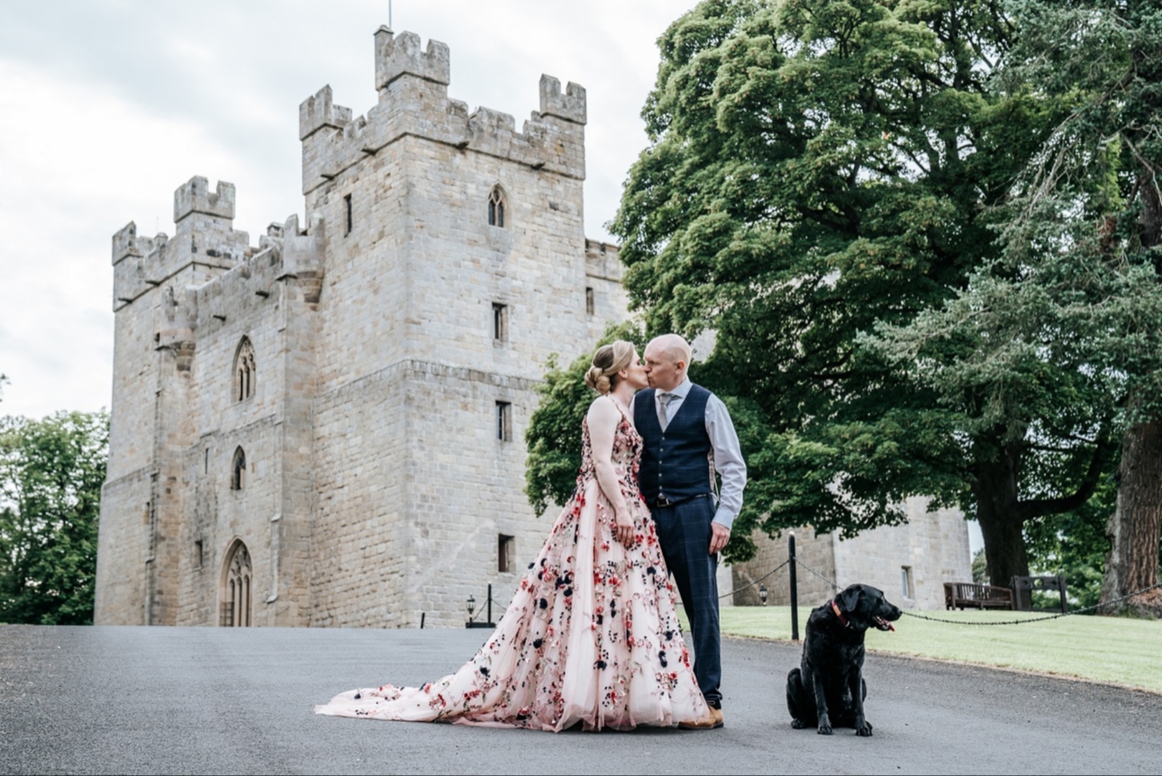 Bride and groom kiss outside Langley Castle with their black dog