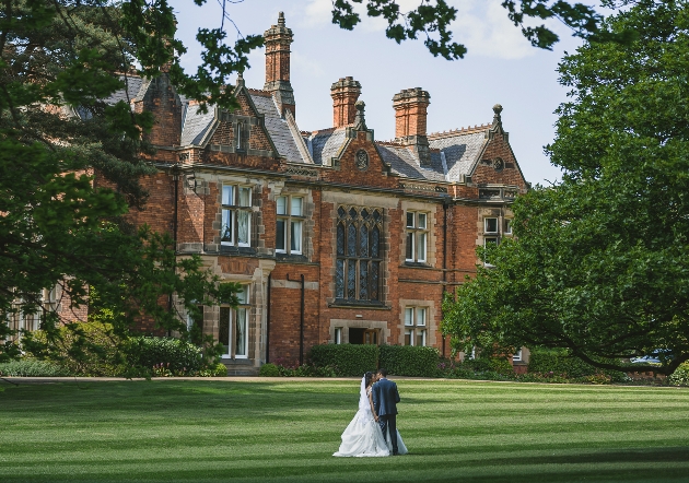 Rockliffe Hall historic house, with large lawns, bride and groom walking on grass