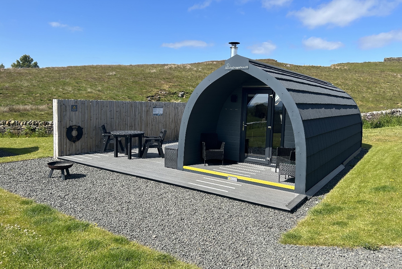 glamping pod grey dome shape, with fence for privacy, hills around it outdoor seating