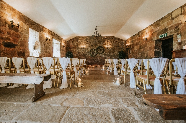 Rows of gold chairs with white fabric tied around them in a stone barn