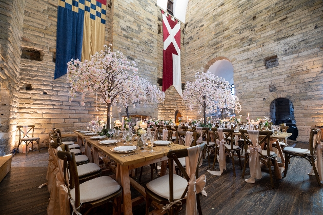 The inside of a castle decorated with tables, chairs and cherry blossom trees as centrepieces