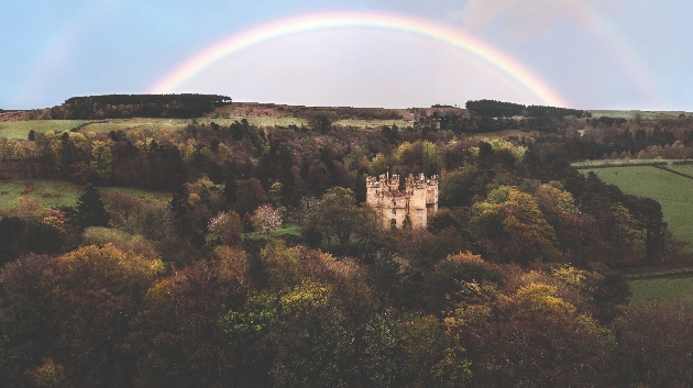 A castle surrounded by acres of forest with a rainbow in the sky