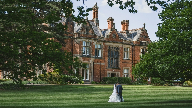 A bride and groom kissing in front of a large mansion