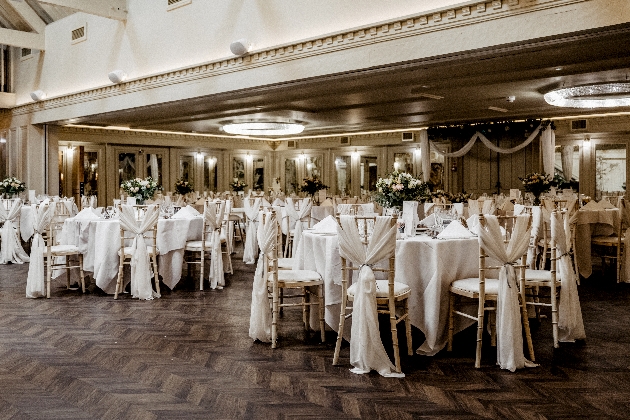 A large modern room with round white tables and chairs with white sashes
