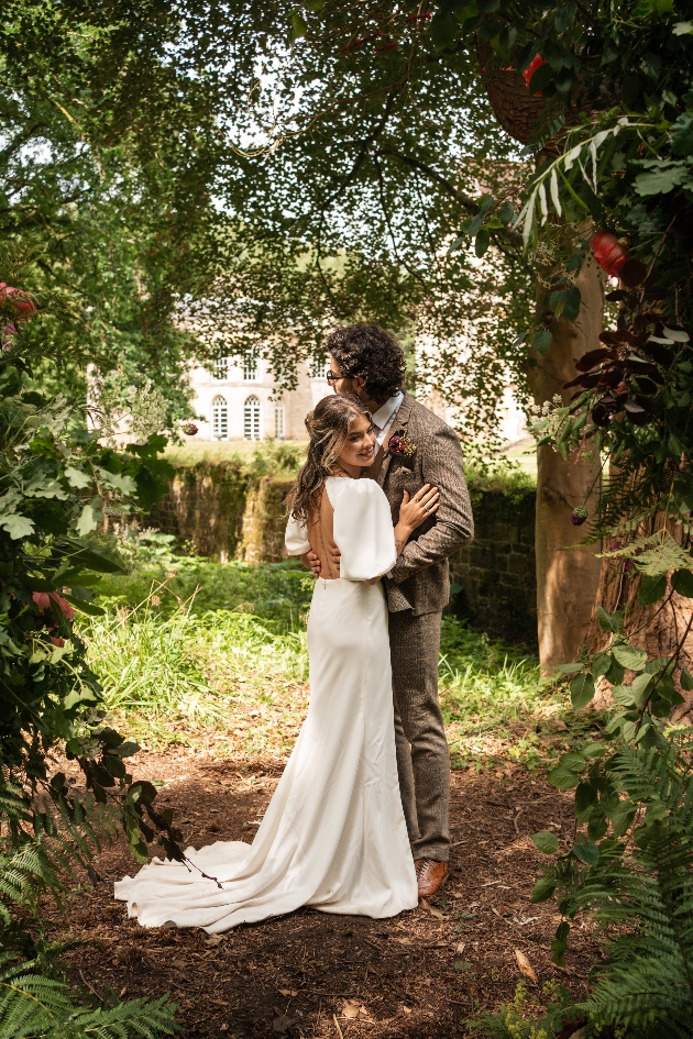 A bride and groom embracing in the middle of a woodland