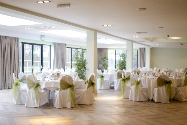 A large room with round tables decorated with green bows