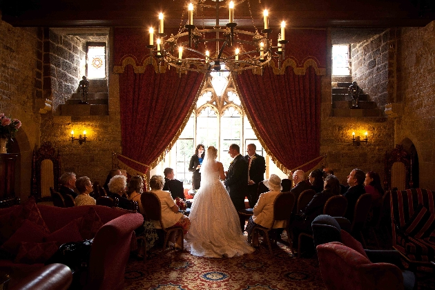 A bride and groom getting married in front of a large window surrounded by friends and family