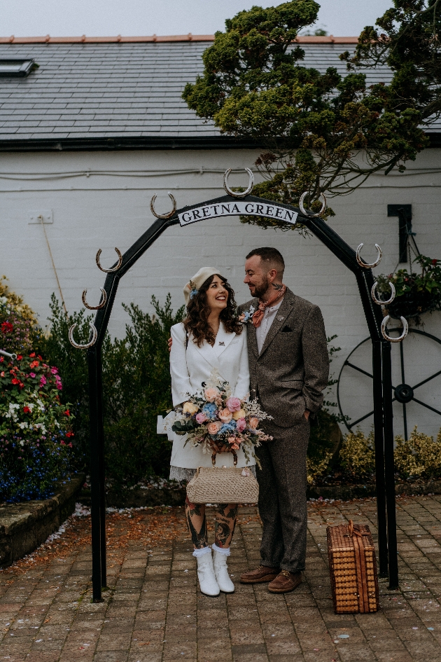 A bride and groom standing underneath a sign that reads Gretna Green
