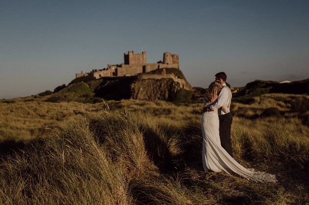 A bride and groom standing in a field with a castle in the distance