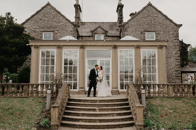 A bride and groom standing in front of a house with lots of windows