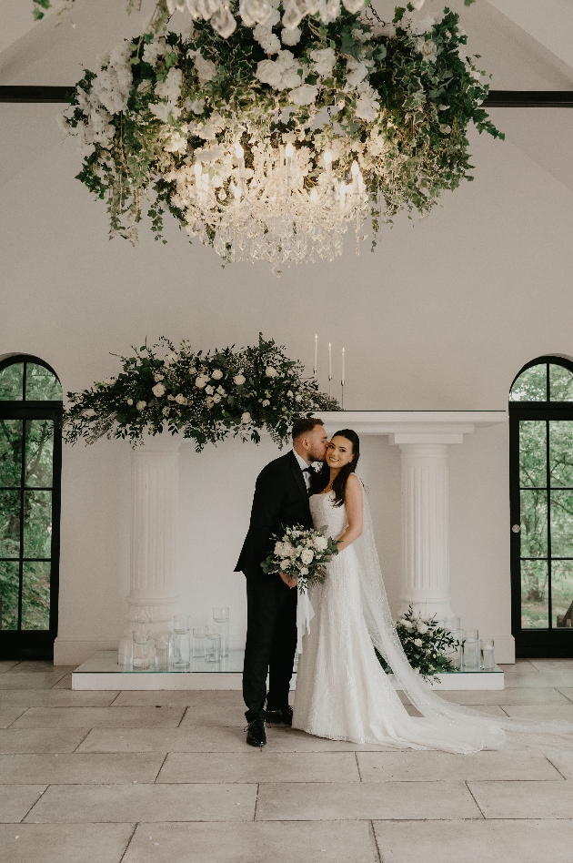 A bride adn groom standing underneath a floral chandelier
