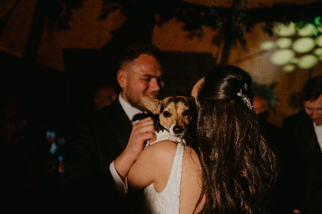 A bride and groom dancing with their dog in between them