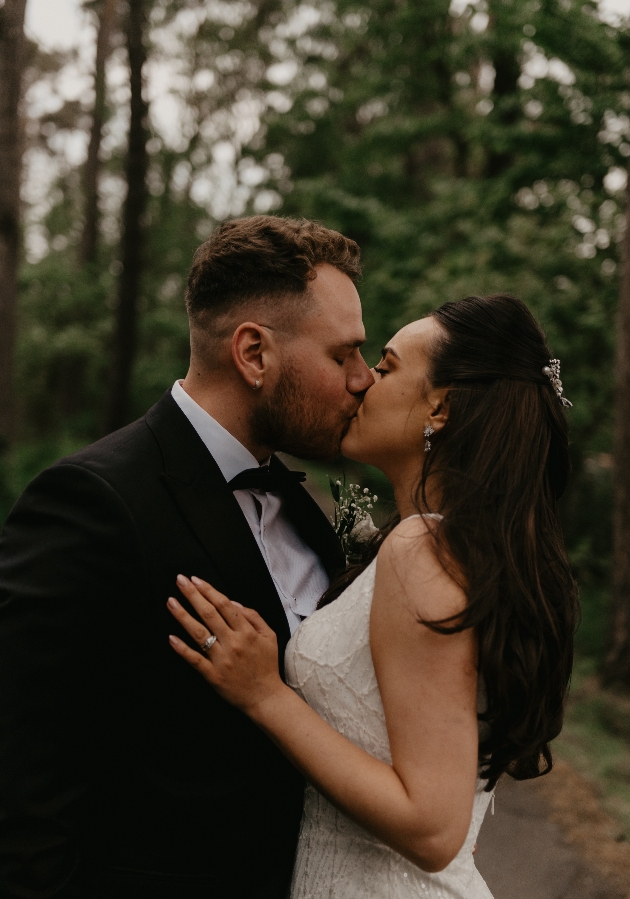 A close up of a bride and groom kissing in the woods